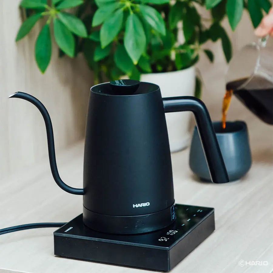 Hario Lyra Wasserkocher Schwarz neben einer Kaffeekanne