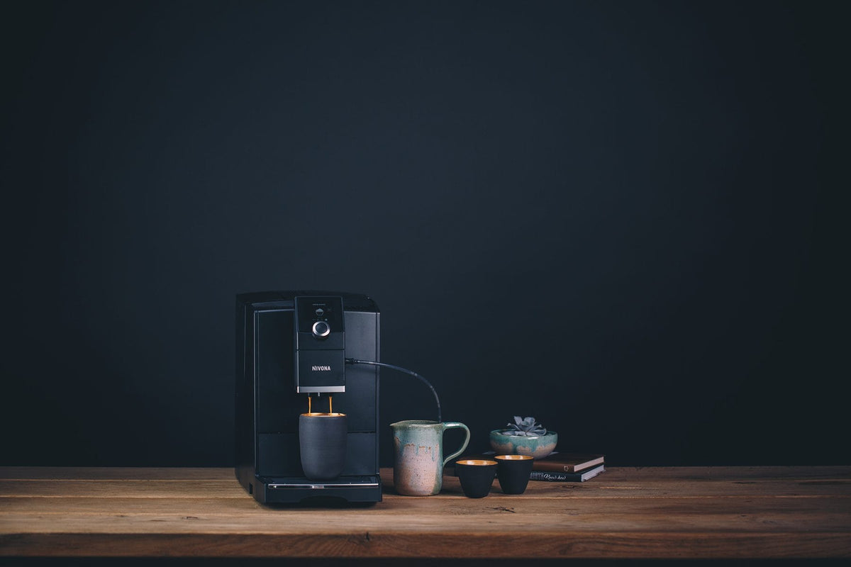 Nivona NICR 7'90 Kaffeevollautomat in Mattschwarz auf einem Holztisch vor dunkler Wand
