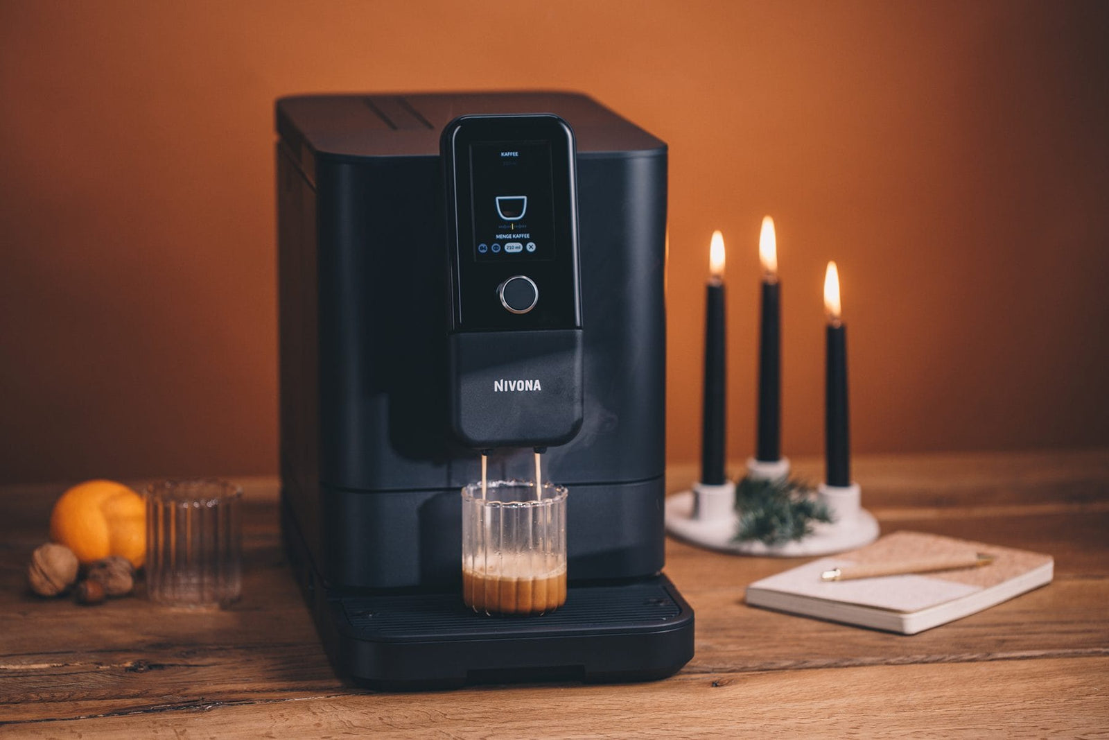 NIVONA NIVO 8'101 Kaffeevollautomat in Schwarz auf einem Holztisch bei Kerzenlicht, ein Latte Macchiato steht bereit
