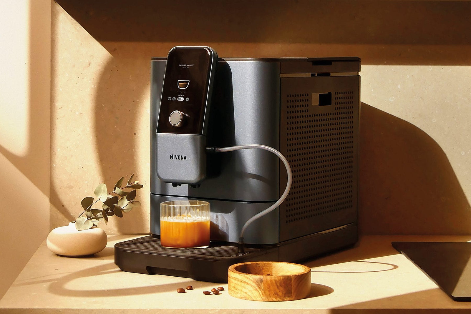 NIVONA NIVO 8'107 bereitet einen Chilled Americano zu, daneben eine Holzschale und Kaffeebohnen
