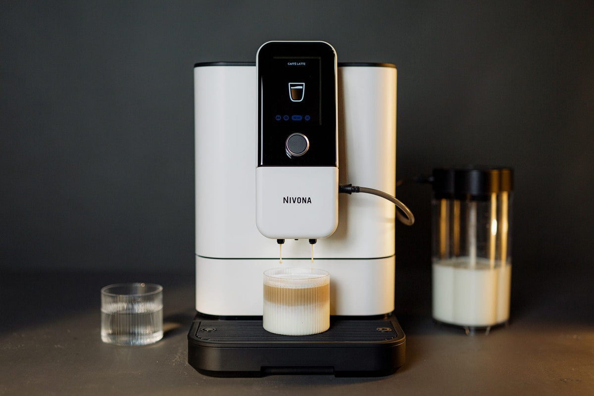 NIVONA NIVO 8'112 Kaffeevollautomat in Weiß bereitet einen Milchkaffee zu, daneben ein Glas Milch