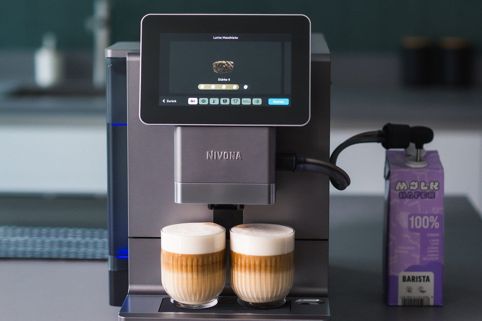 NIVONA Kaffeevollautomat bereitet zwei Latte Macchiato mit Hafermilch zu, das Display zeigt Stärke 4