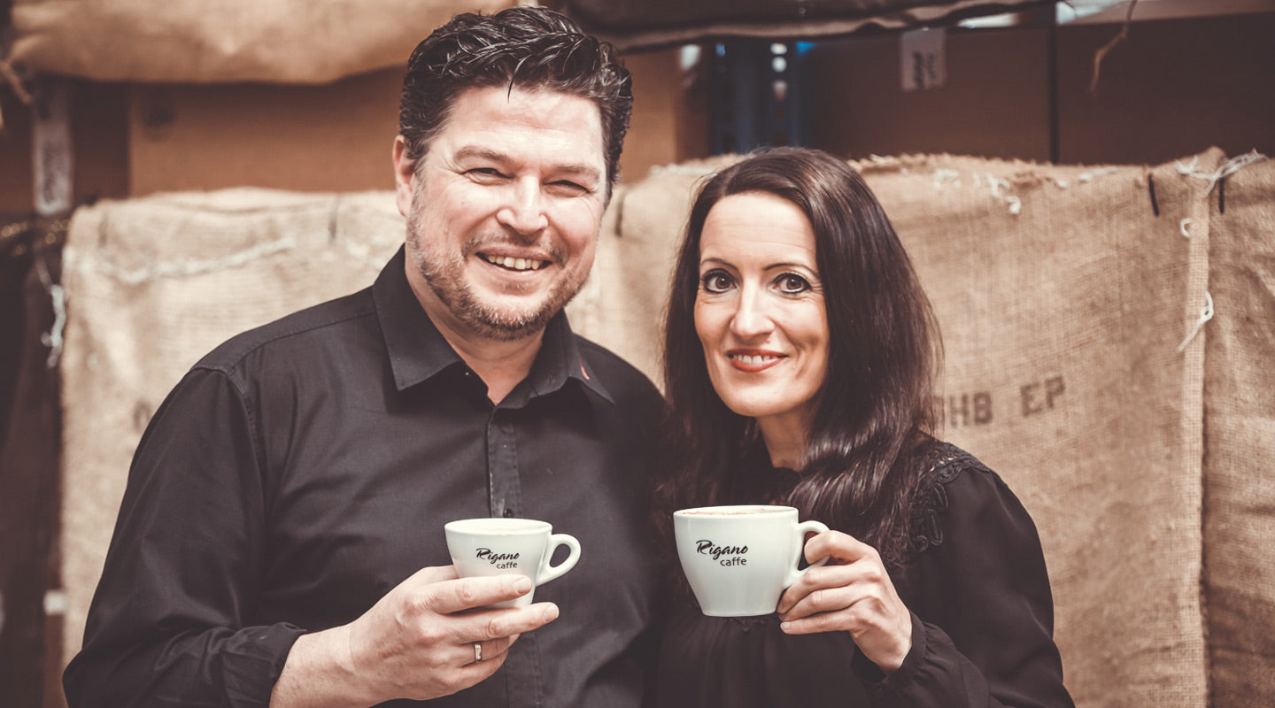 Lorenzo und Stephanie Rigano mit Espressotassen vor Rohkaffeesäcken